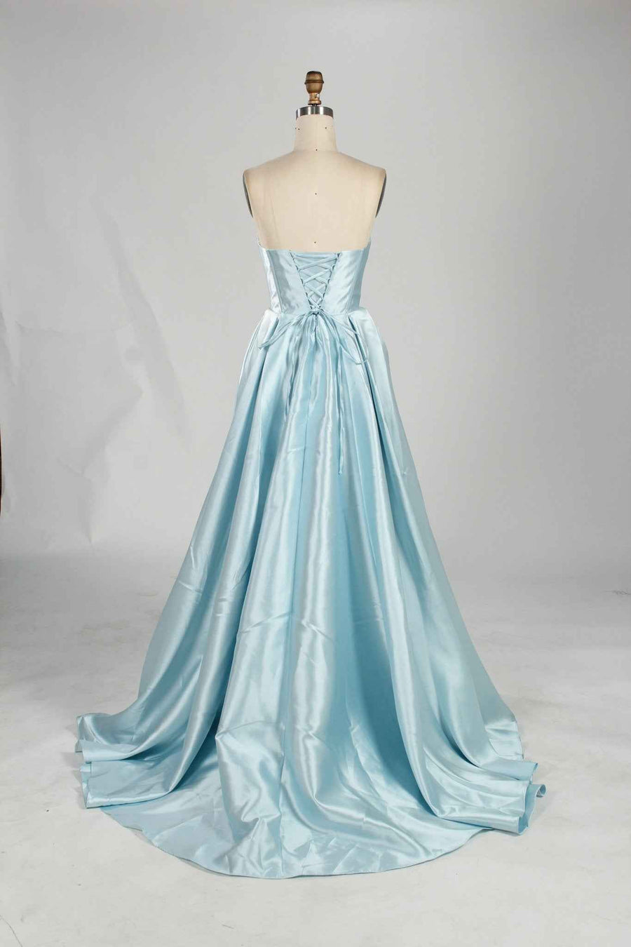 Carmen Ball Gown in light blue satin with strapless lace-up back and pleated full skirt. Elegant formal dress with pockets for prom or red carpet events.