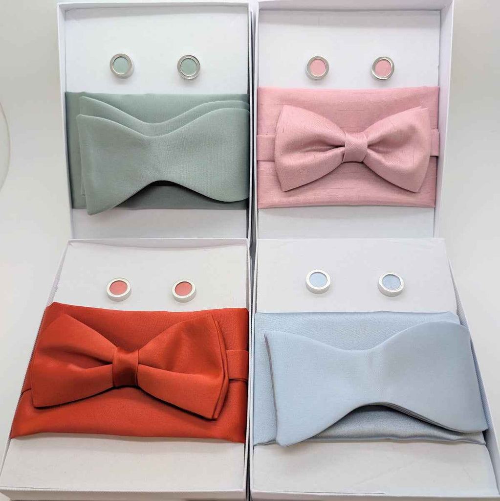 Set of four wedding bow ties in pastel and bold colors with matching pocket squares and cufflinks, perfect for groomsmen accessories and formal attire.