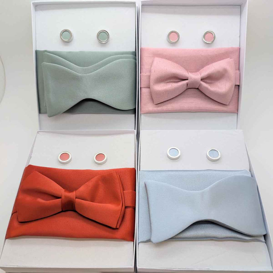 Set of four wedding bow ties in pastel and bold colors with matching pocket squares and cufflinks, perfect for groomsmen accessories and formal attire.