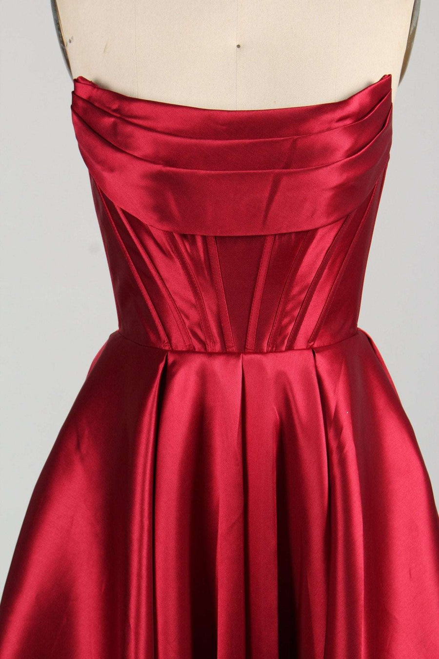 Close-up of Carmen wine red satin ball gown showing strapless bodice with pleated detailing and structured seams. Elegant formal dress with pockets.