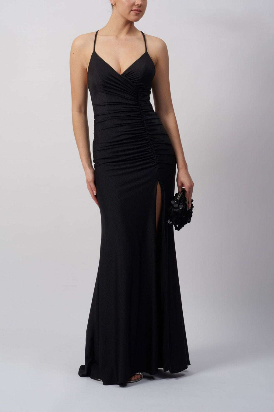 Model wearing a black pleated jersey tie back dress by Mascara London, featuring a figure-hugging design with a high slit and rouched detailing