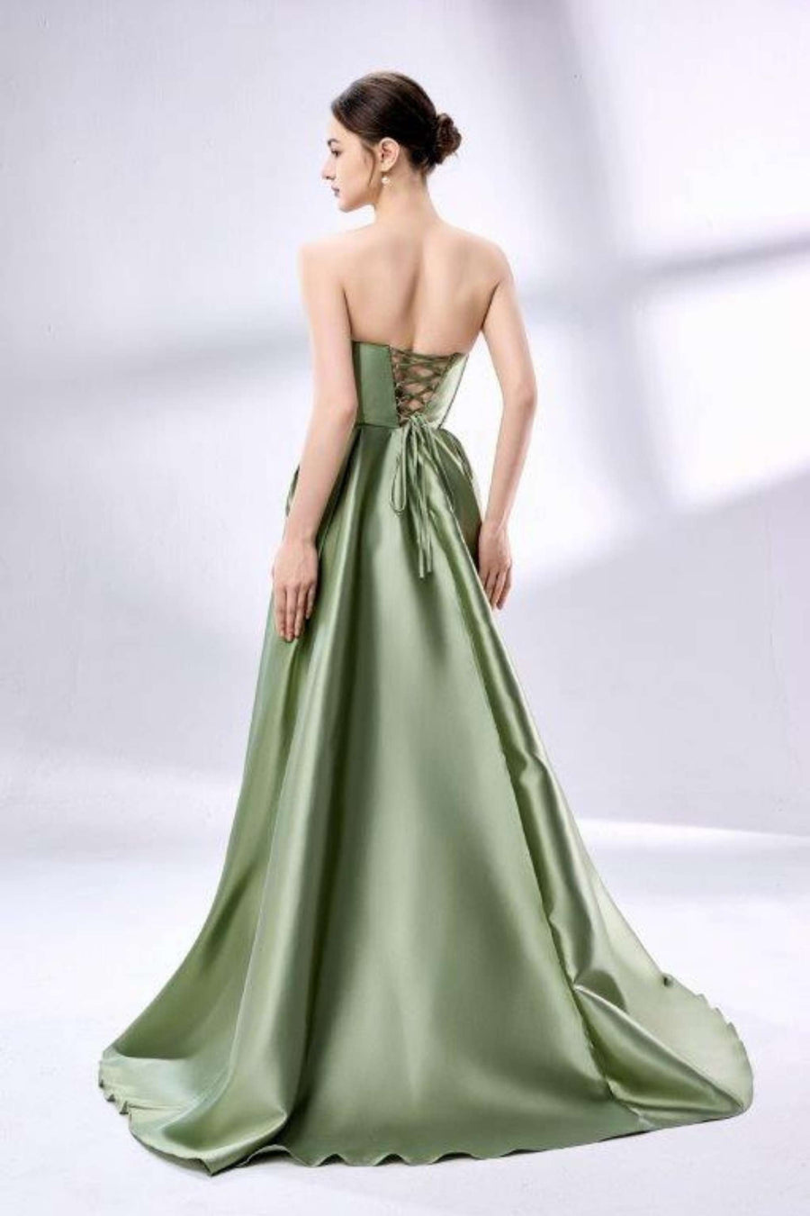 Back view of Jessica Stuart sage green satin ball gown with lace-up corset and flowing train. Elegant strapless formal dress with pockets for prom or events.
