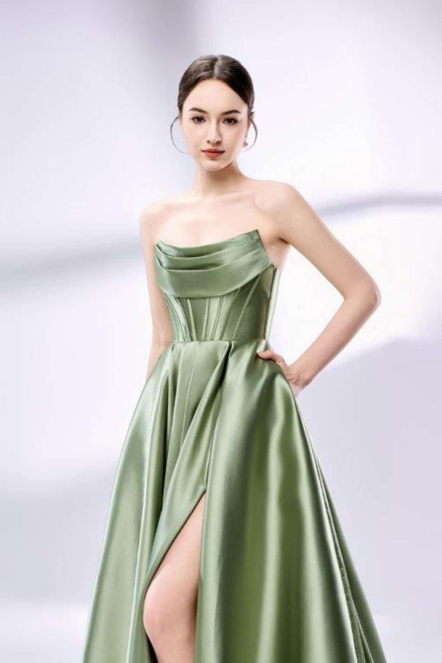 Jessica Stuart sage green satin ball gown with pockets featuring a strapless neckline, pleated bodice, and thigh-high slit. Ideal for prom or formal events.