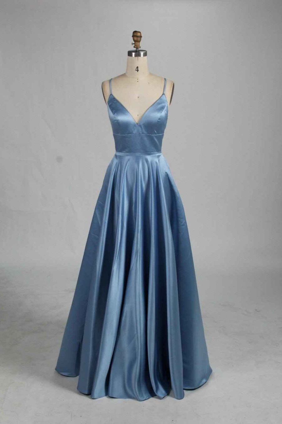 AVA Open Back Dusty Blue Prom Dress with V-neck and full skirt. Features thin straps, lace-up back, and hidden pockets for formal occasions.