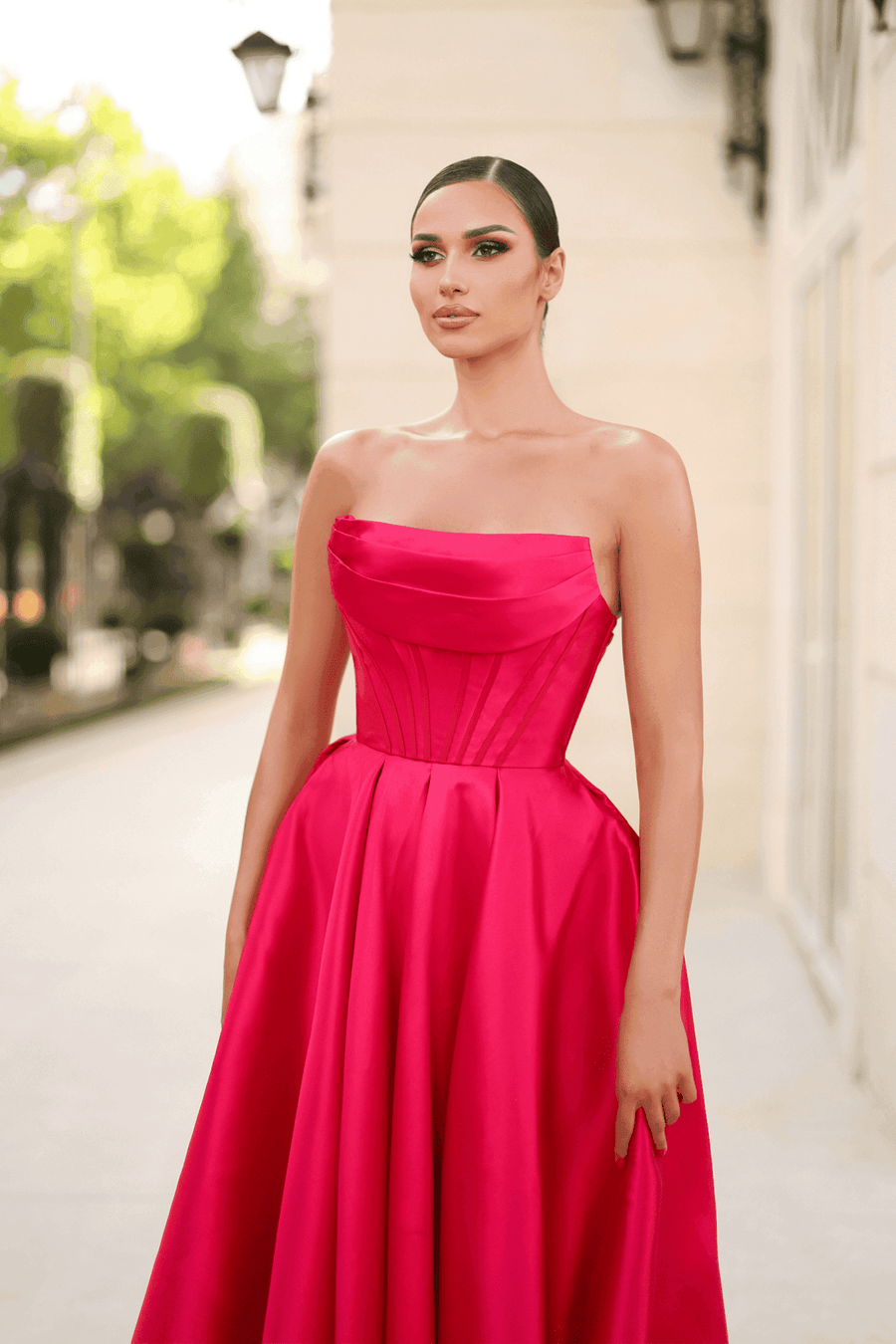 Carmen Ball Gown in wine red satin with structured strapless bodice, lace-up back, and full skirt with pockets. Elegant choice for prom or formal events.